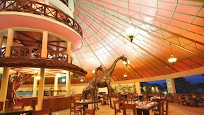 A spacious indoor dining area with a high ceiling, multiple dining tables, and a central decorative sculpture.