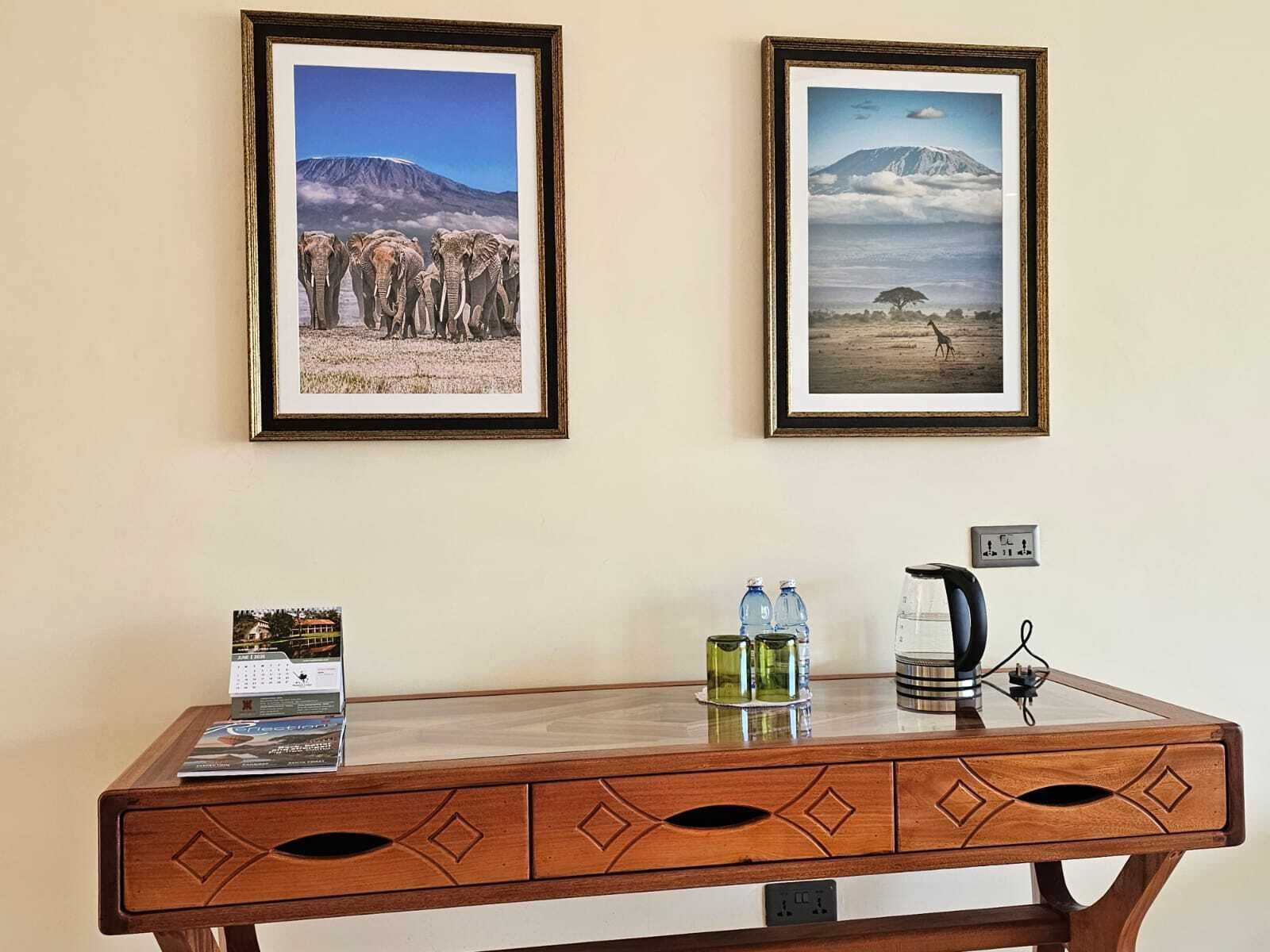 Un escritorio de madera con un marco que contiene una foto de elefantes, un marco con una foto de una montaña, un calendario y un hervidor.