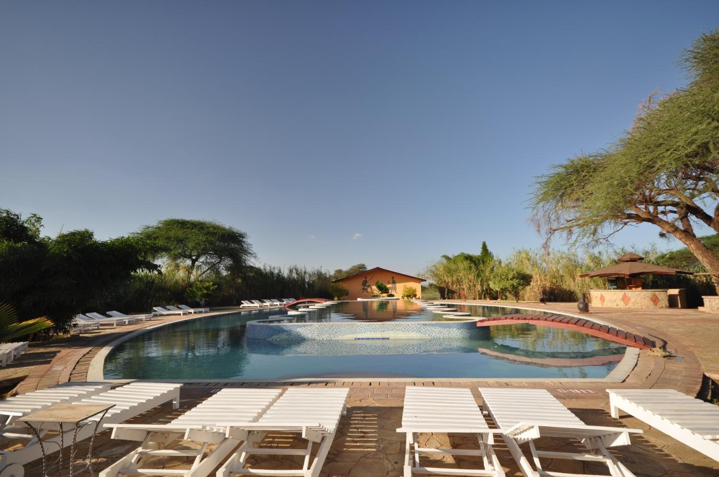 Piscina com espreguiçadeiras e um pequeno edifício ao fundo.
