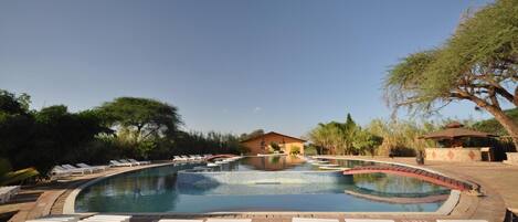 Piscina com espreguiçadeiras e um pequeno edifício ao fundo.