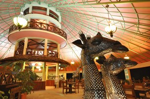 Una estructura de varios niveles con un atrio central, una gran escultura de jirafa y zonas de comedor con mesas y sillas.