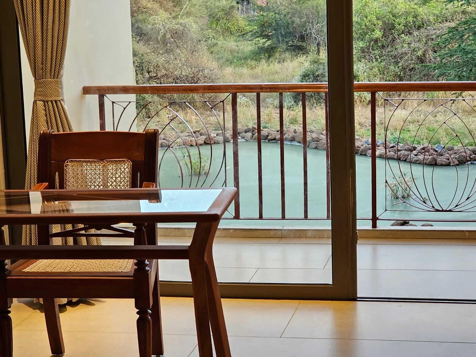 Een balkon met uitzicht op een rivier, een eettafel met stoelen en een gordijn met patroon.