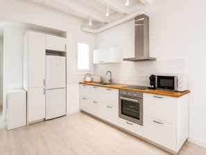 Uma cozinha moderna com armários brancos, bancada de madeira, forno embutido, micro-ondas e coifa de aço inoxidável.