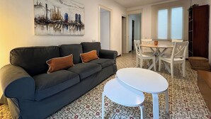 Ein modernes Wohnzimmer mit einer schwarzen Couch, einem weißen Couchtisch und einem Essbereich mit weißen Stühlen und einem kleinen Tisch.