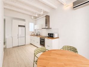 A modern kitchen with white cabinetry, a wooden countertop, a built-in oven, and a microwave. There is a round wooden table with chairs.