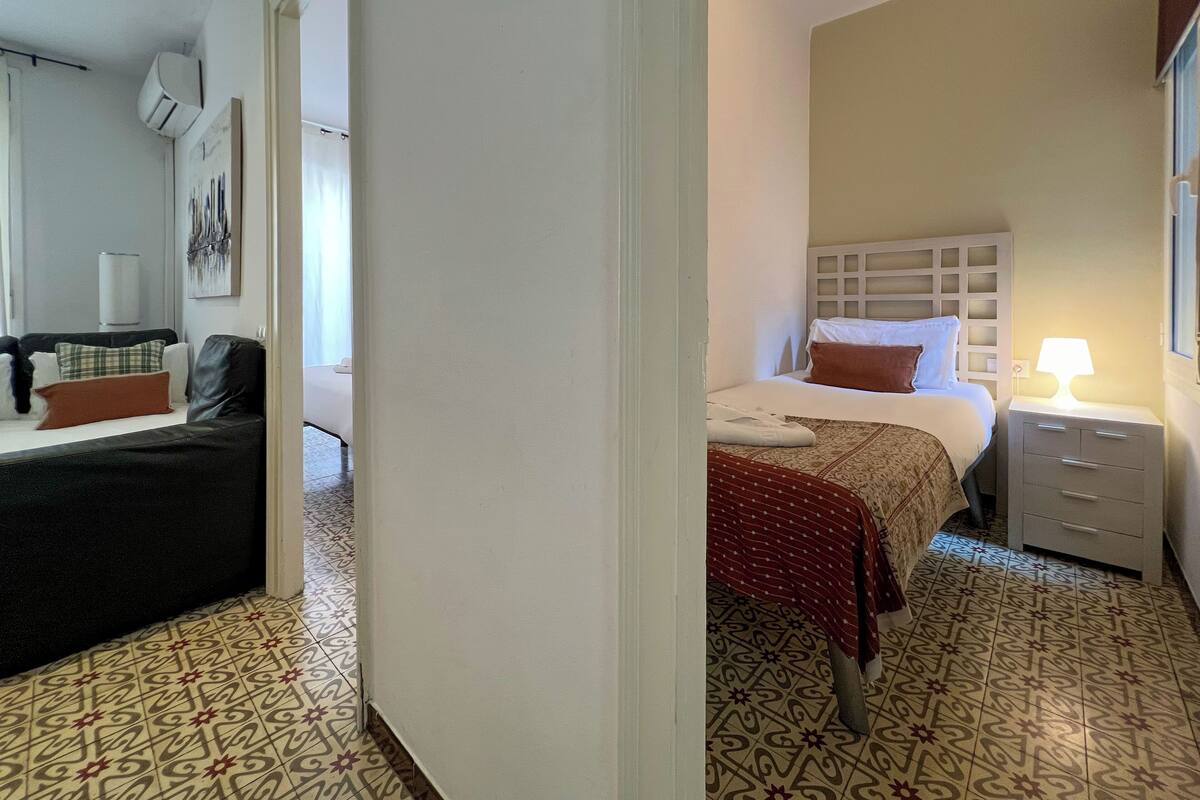 Una habitación de hotel con cama, mesita de noche y un sofá en la zona de estar contigua.