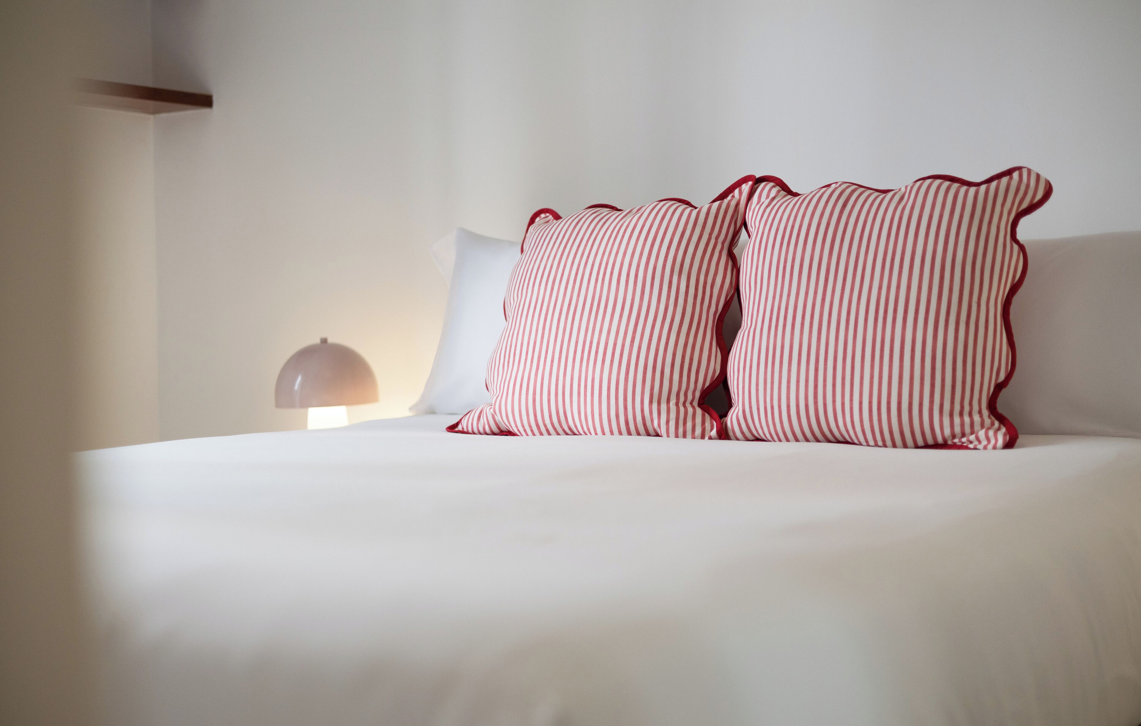 Un lit bien fait, avec deux oreillers à rayures et un oreiller blanc uni, une lampe de chevet et un mur blanc.