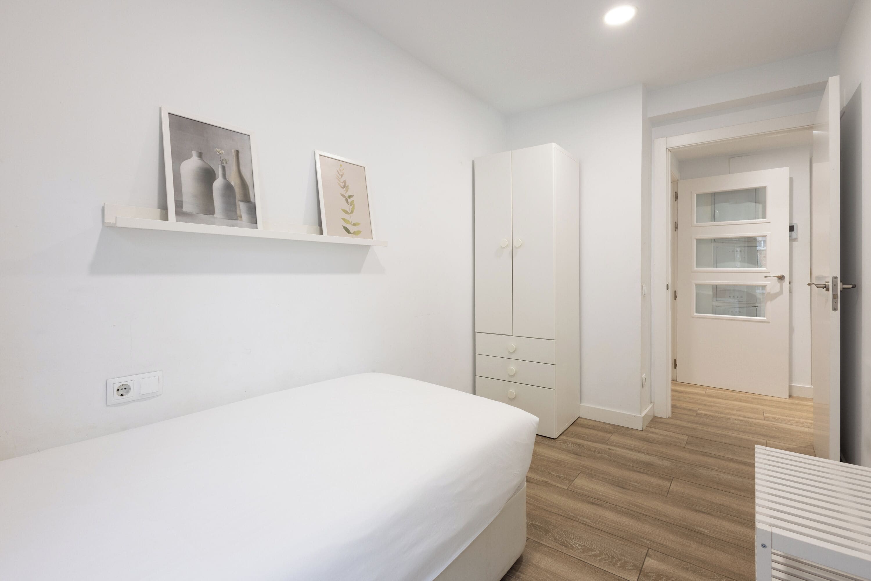 Un dormitorio con una cama, un armario y una estantería con obras de arte enmarcadas.