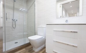 Een moderne badkamer met een douche met glazen wand, een toilet en een wastafel met lades.