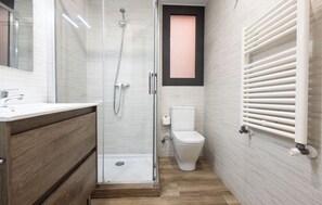 Ein modernes Badezimmer mit einer gläsernen Duschkabine, einem Holzausziehtisch, einer Toilette und einem Heizkörper.