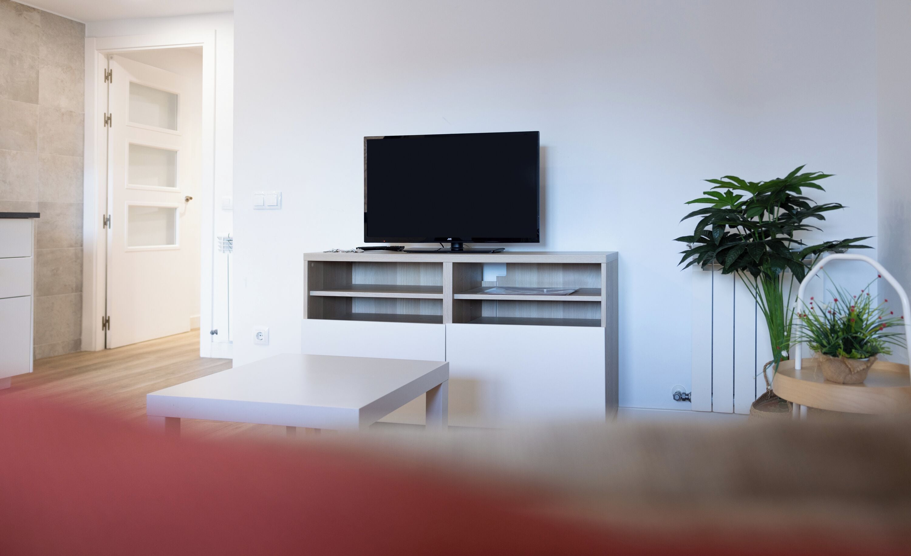 A modern living room with a flat-screen TV on a wooden stand, a white coffee table, and a potted plant.