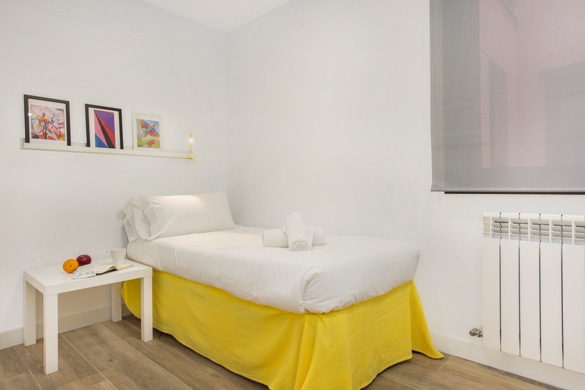 Un dormitorio con una cama, una mesita de noche, un radiador y tres cuadros en la pared.