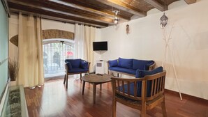 A living room with a wooden ceiling, a blue sofa, a wooden chair, a small table, and a TV mounted on the wall. - Stay U-nique Apartments Plaça Universitat (Barcelona)
