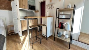 Une cuisine compacte avec des meubles en bois, un four à micro-ondes encastré, un grille-pain et une étagère contenant des ustensiles de cuisine.
