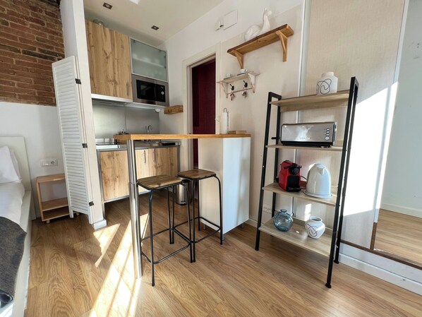 A compact kitchen with wooden cabinets, a built-in microwave, a toaster, and a shelf with kitchenware.