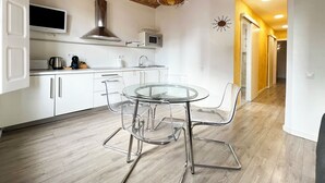 A modern kitchen with white cabinetry, a stainless steel range hood, a microwave, and a glass dining table with chairs. - Stay U-nique Apartments Fontrodona (Barcelona)