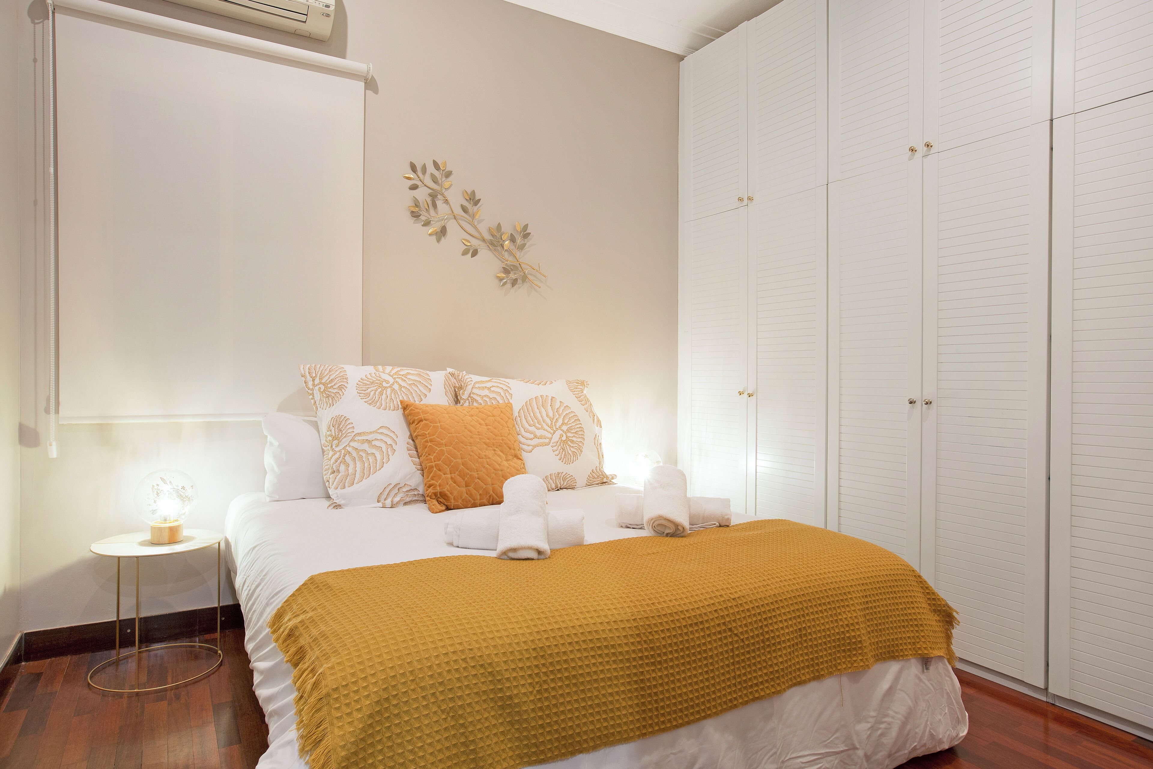 Une chambre bien rangée, avec un lit, une table de chevet dotée d’une lampe, une armoire et un climatiseur fixé au mur.