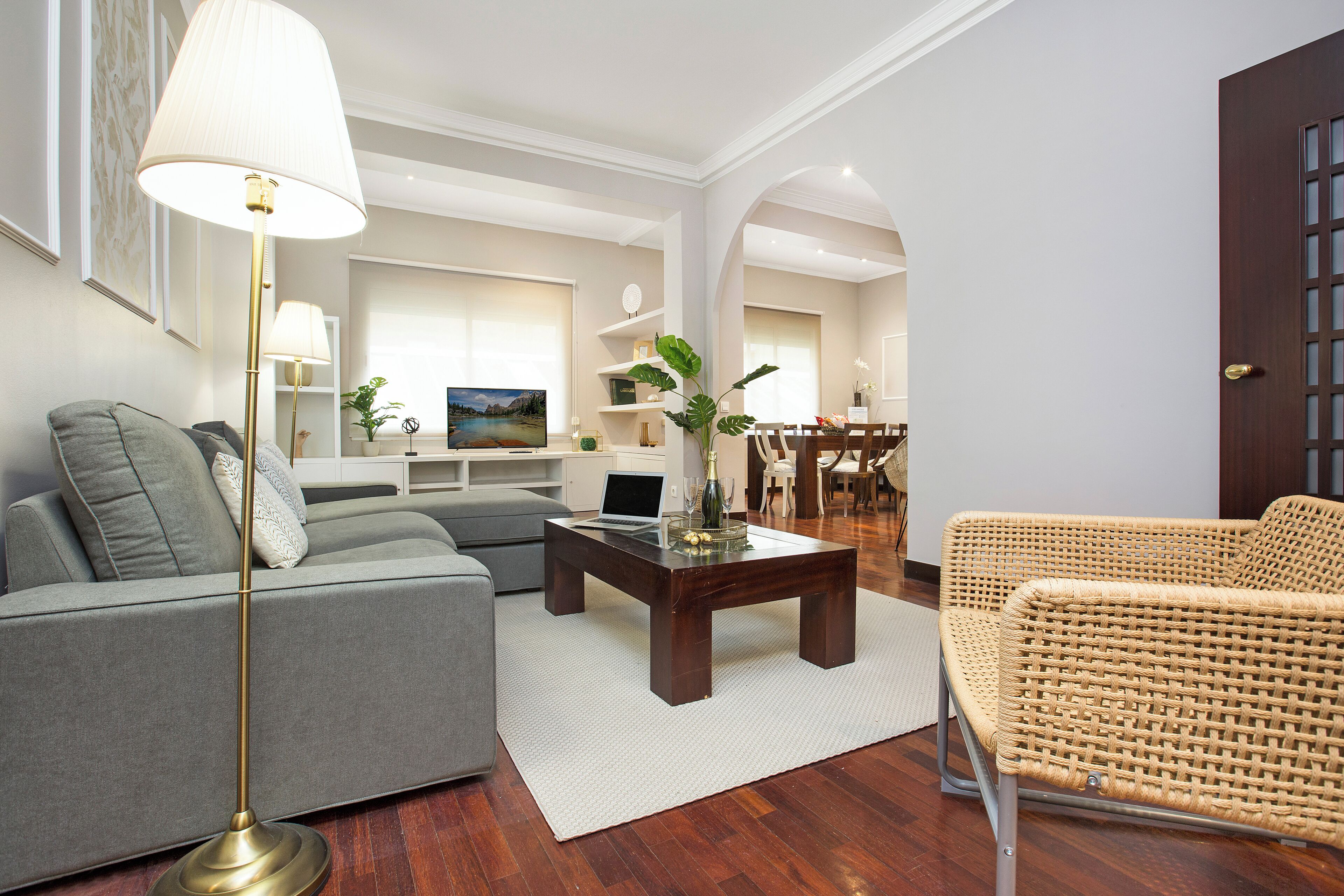 A modern living room with a grey sofa, a wicker chair, a wooden coffee table, and a floor lamp.
