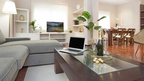 A modern living room with a sofa, a glass coffee table, a laptop, and a dining area with chairs and a table. - Stay U-nique Apartments Calvet (Barcelona)