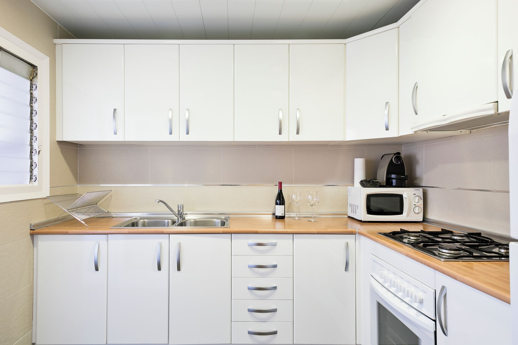 A kitchen with white cabinets, a wooden countertop, a sink, a microwave, a stove, and a wine bottle.