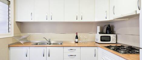 A kitchen with white cabinets, a wooden countertop, a sink, a microwave, a stove, and a wine bottle.