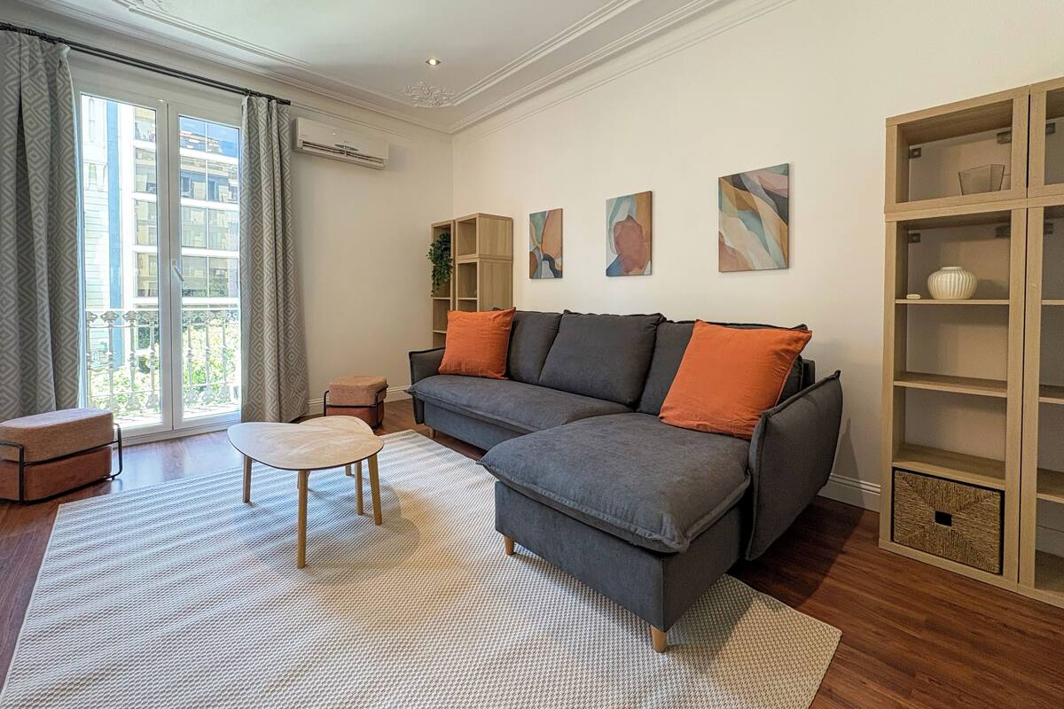 Una sala de estar moderna con un sofá seccional gris, una mesita redonda y una estantería.
