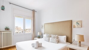 A modern bedroom with a large bed, a view of the city through the window, a radiator, and a small table with a lamp. - Stay U-nique Apartments Rambla Catalunya (Barcelona)