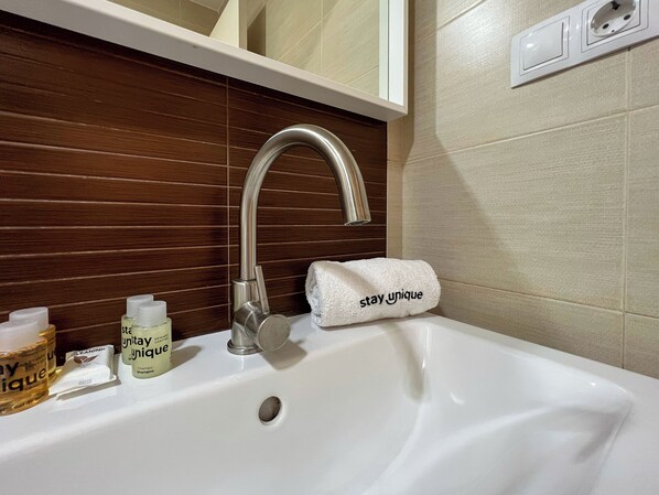 Un lavabo de salle de bain avec un robinet moderne, une serviette ornée de l’inscription « restez unique », et des articles de toilette posés sur le comptoir.