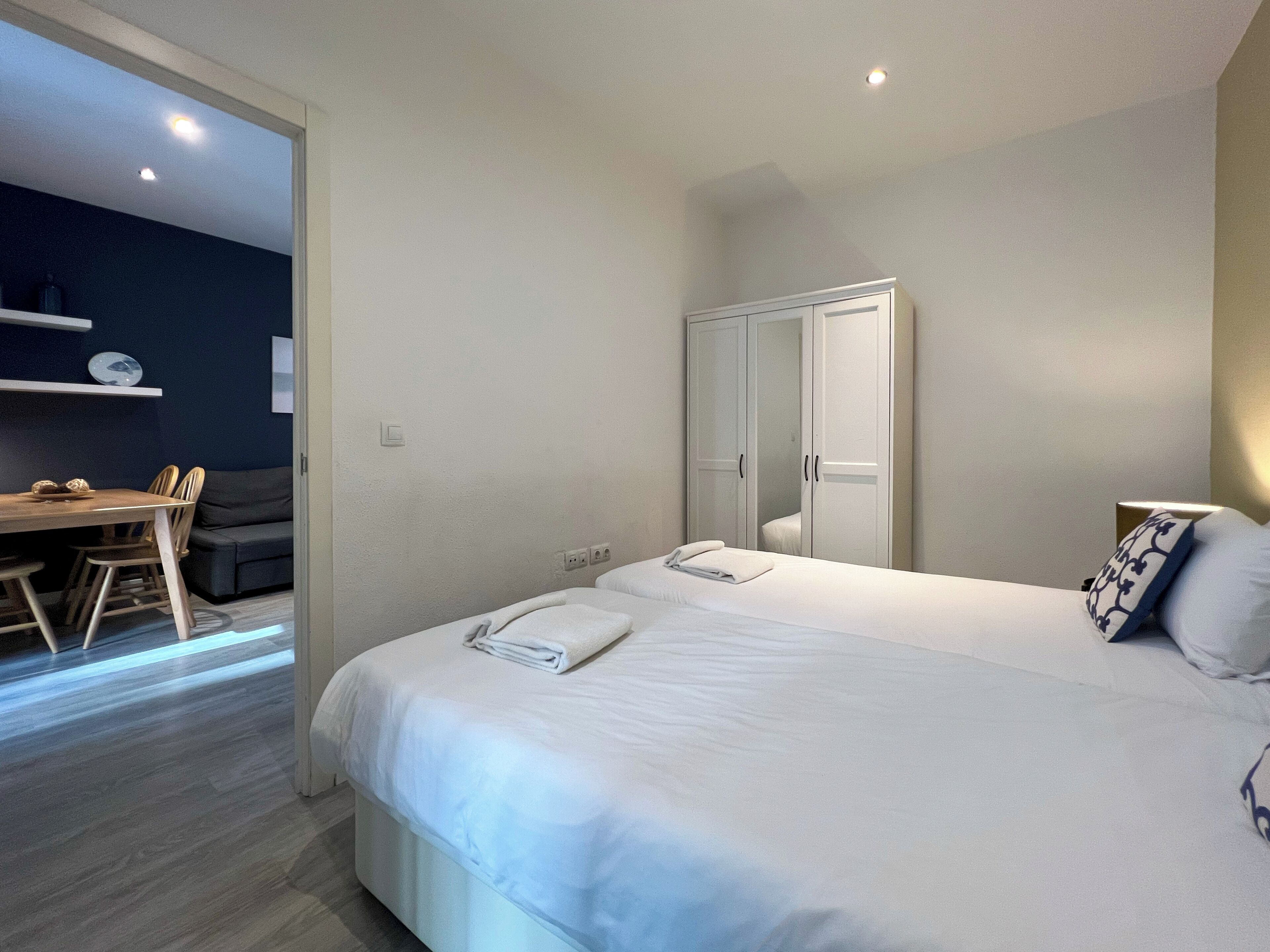 Un dormitorio moderno con una cama grande, un armario y una pequeña zona de comedor con mesa y sillas.