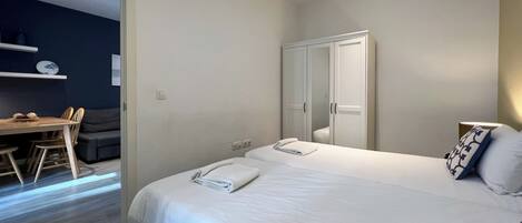 Un dormitorio moderno con una cama grande, un armario y una pequeña zona de comedor con mesa y sillas.