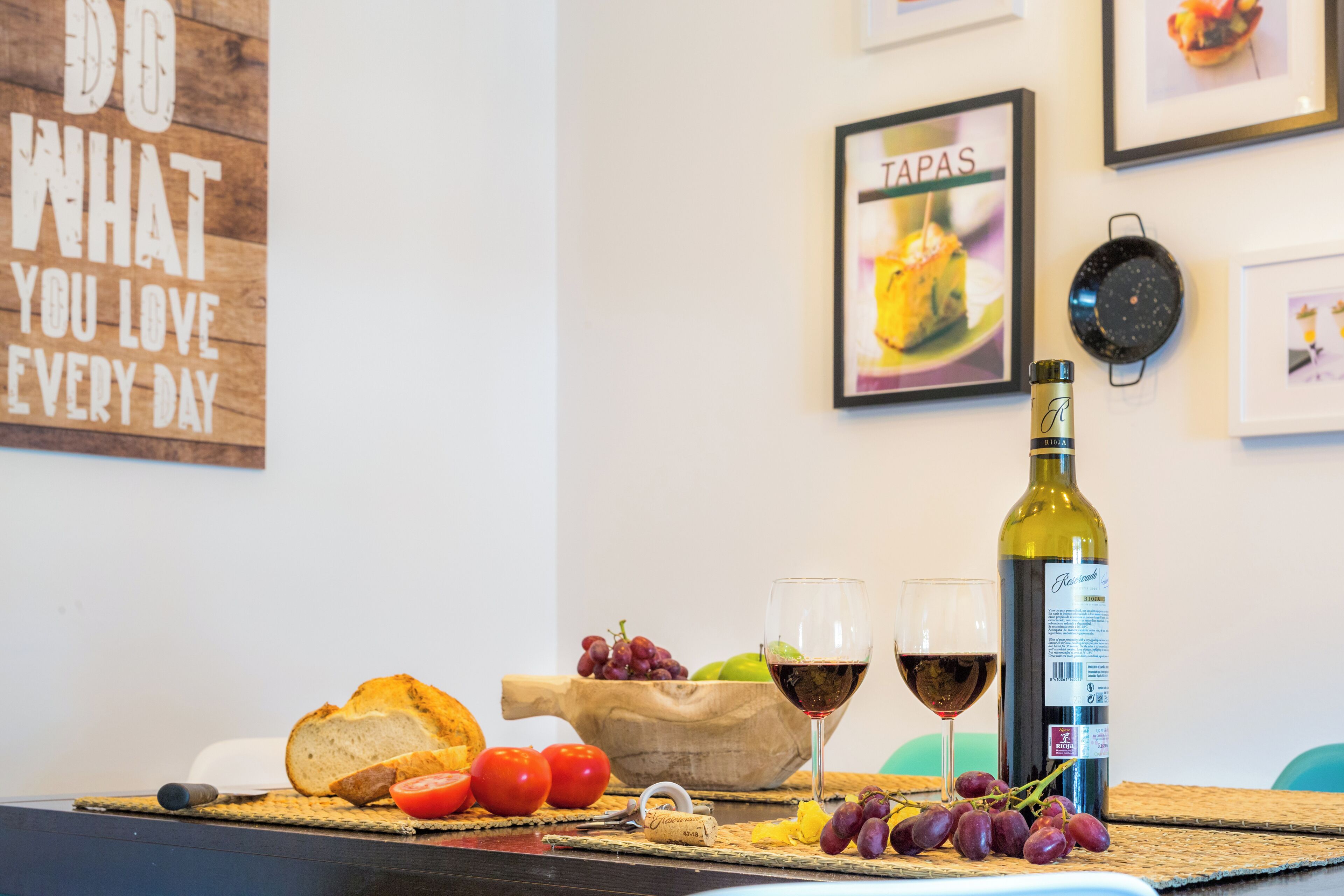 Een tafel met brood, tomaten, druiven, een fles wijn en een kurkentrekker.