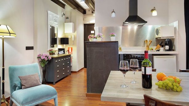 A modern kitchen with a dining area, wooden flooring, and a blue armchair. - Stay U-nique Apartments Carretes (Barcelona)