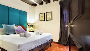A neatly made bed with a teal headboard, white linens, and several pillows. There are two framed pictures on the wall, a lamp on a bedside table, and a wooden floor. - Stay U-nique Apartments Carretes (Barcelona)