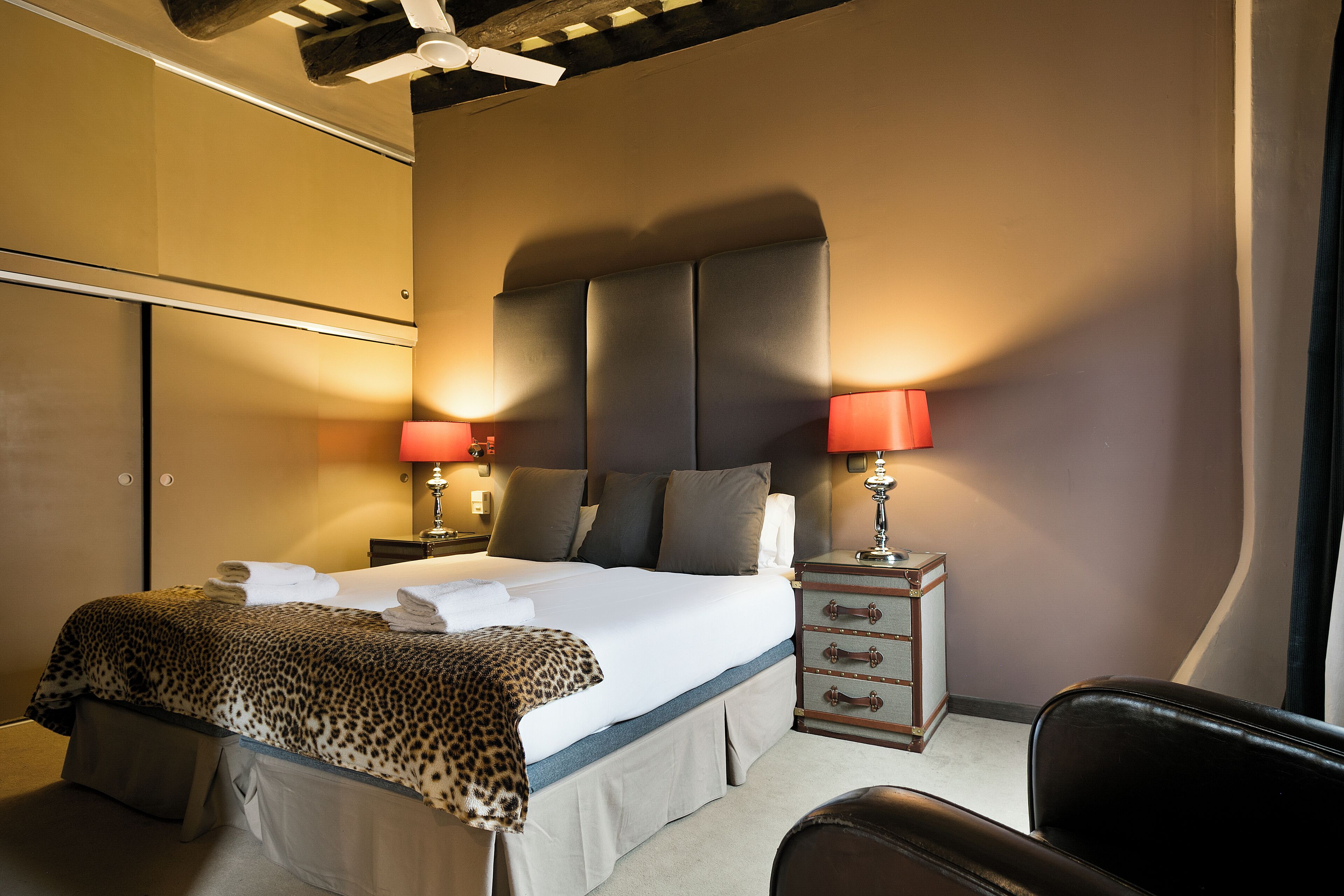 A hotel room with a large bed, two bedside tables with lamps, a chair, and a wardrobe.