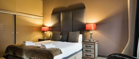 A hotel room with a large bed, two bedside tables with lamps, a chair, and a wardrobe.