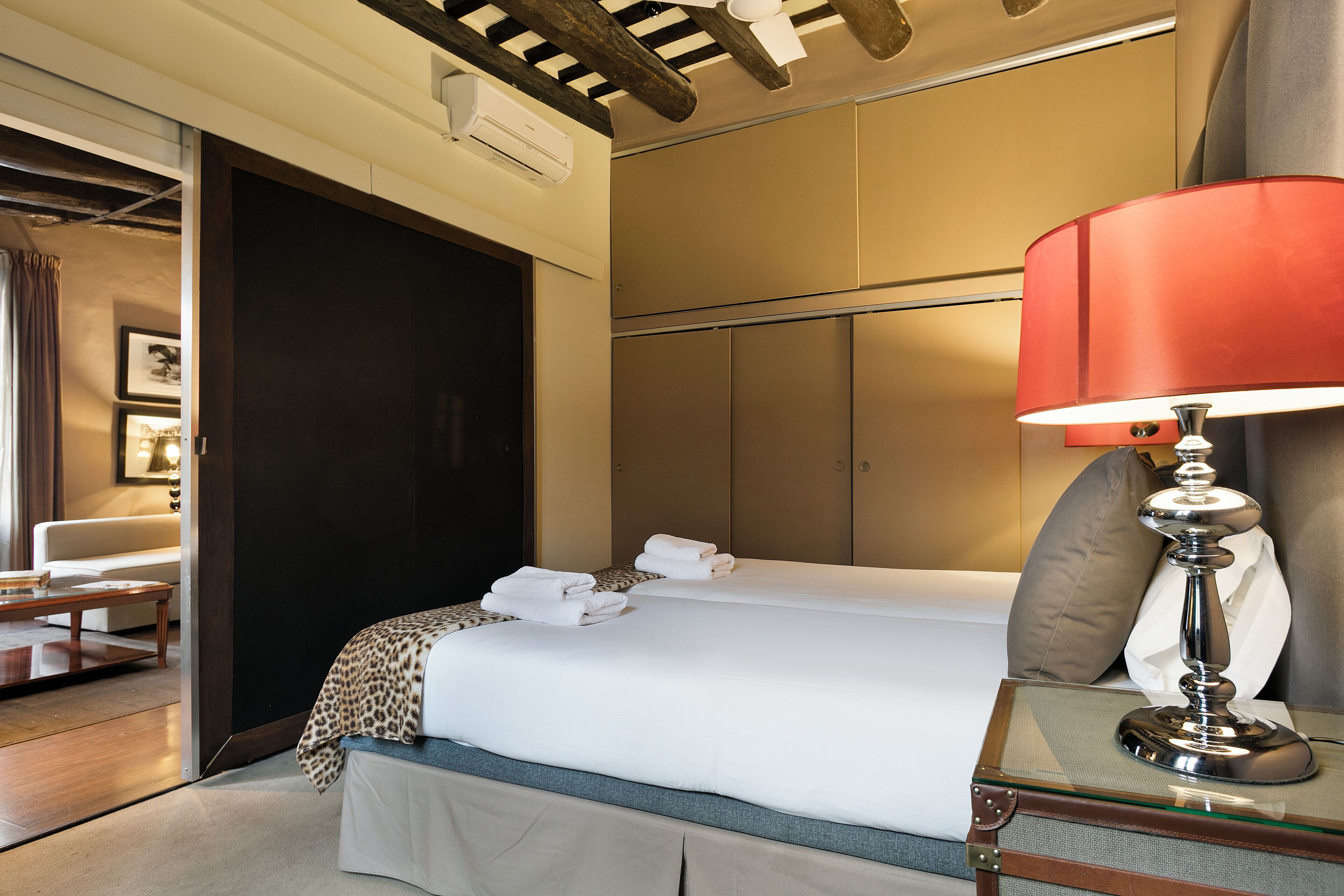Habitación de hotel con cama, mesita de noche con lámpara, una silla y un escritorio con lámpara.