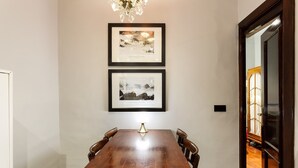 Un comedor con una mesa y sillas de madera, dos cuadros en la pared y una araña.