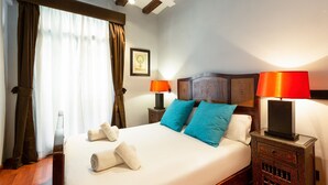 Una cama bien hecha con dos almohadas, dos toallas enrolladas y dos lámparas de noche.
