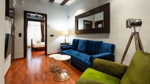 Una sala de estar moderna con un sofá azul, un sillón verde y piso de madera. Hay una lámpara sobre una mesita auxiliar y un espejo en la pared.