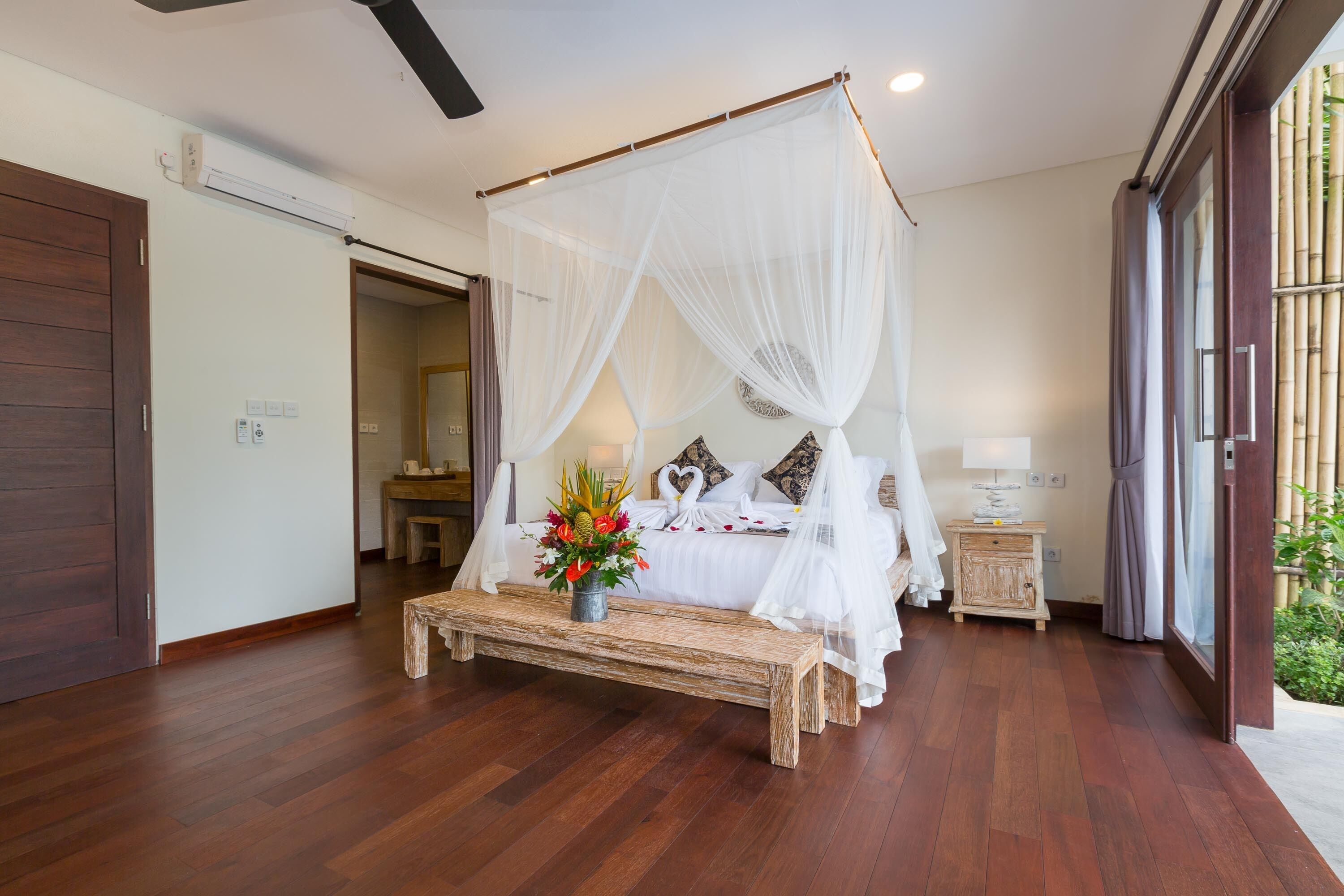 Una camera da letto con un letto a baldacchino, una panca di legno e un comodino con un vaso di fiori.