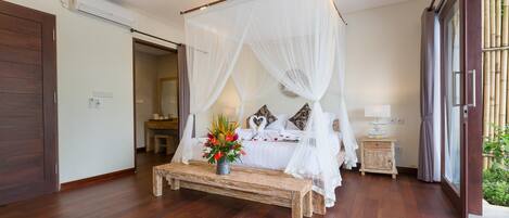 A bedroom with a four-poster bed, a wooden bench, and a bedside table with a vase of flowers.