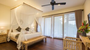 A bedroom with a four-poster bed, wooden flooring, a ceiling fan, and a large window with curtains.