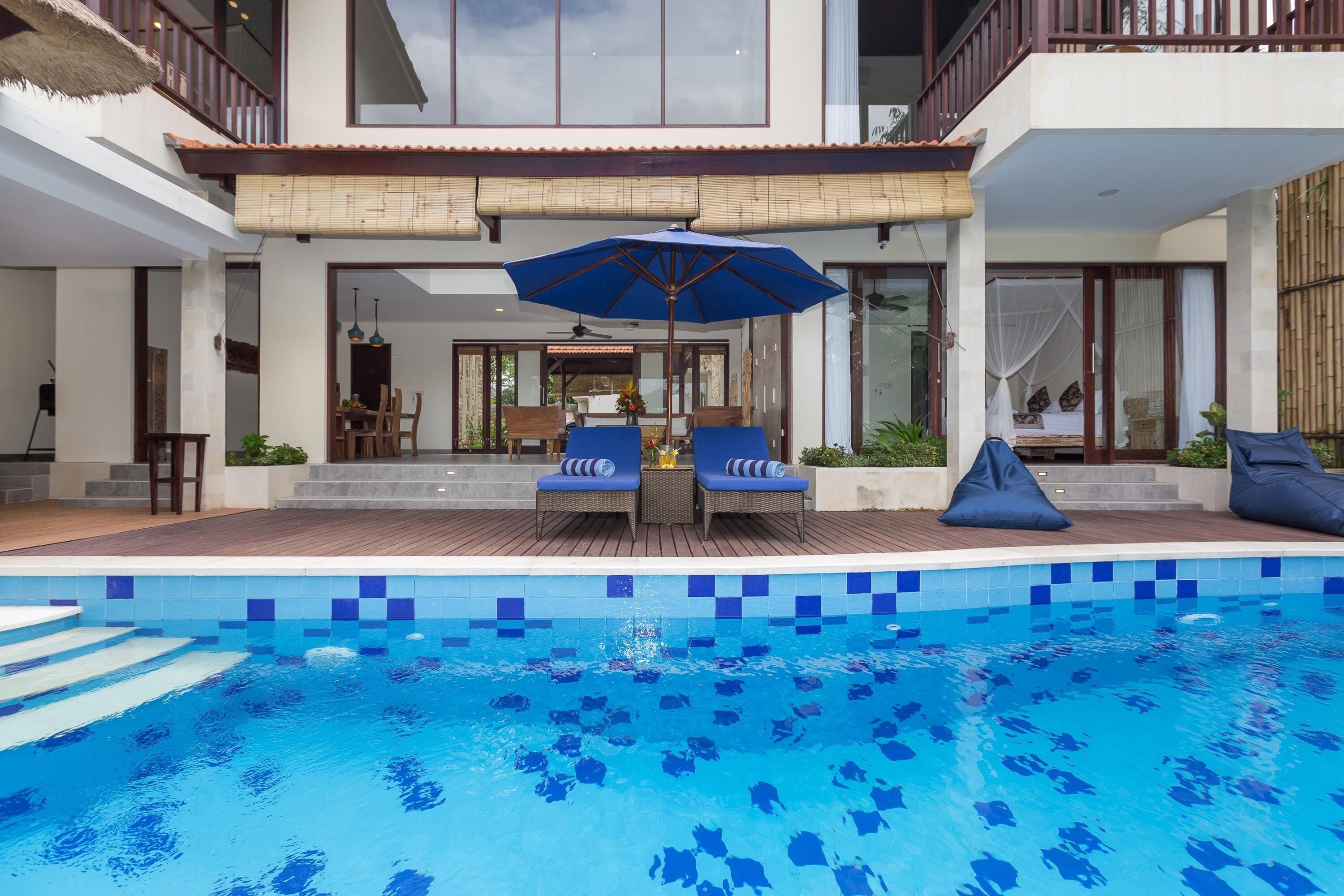 Un espace piscine moderne avec une piscine à l’eau d’un bleu limpide, deux chaises longues et un grand parasol.