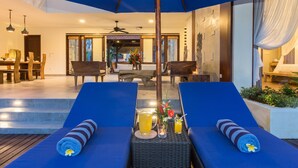 A poolside area with two lounge chairs, a table with drinks, and a ceiling fan.