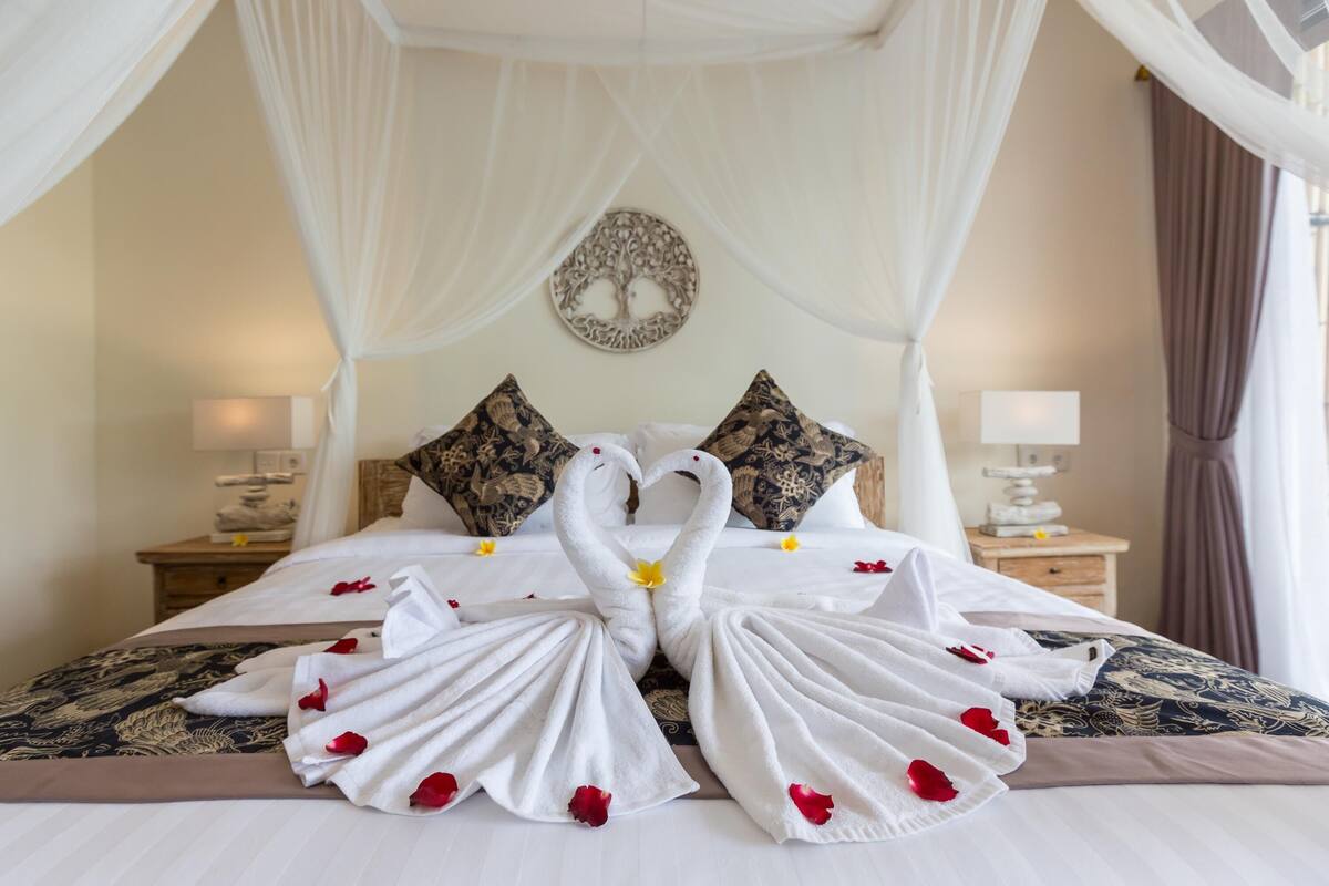 A hotel room with a bed featuring a canopy, decorative pillows, and a wall art piece.