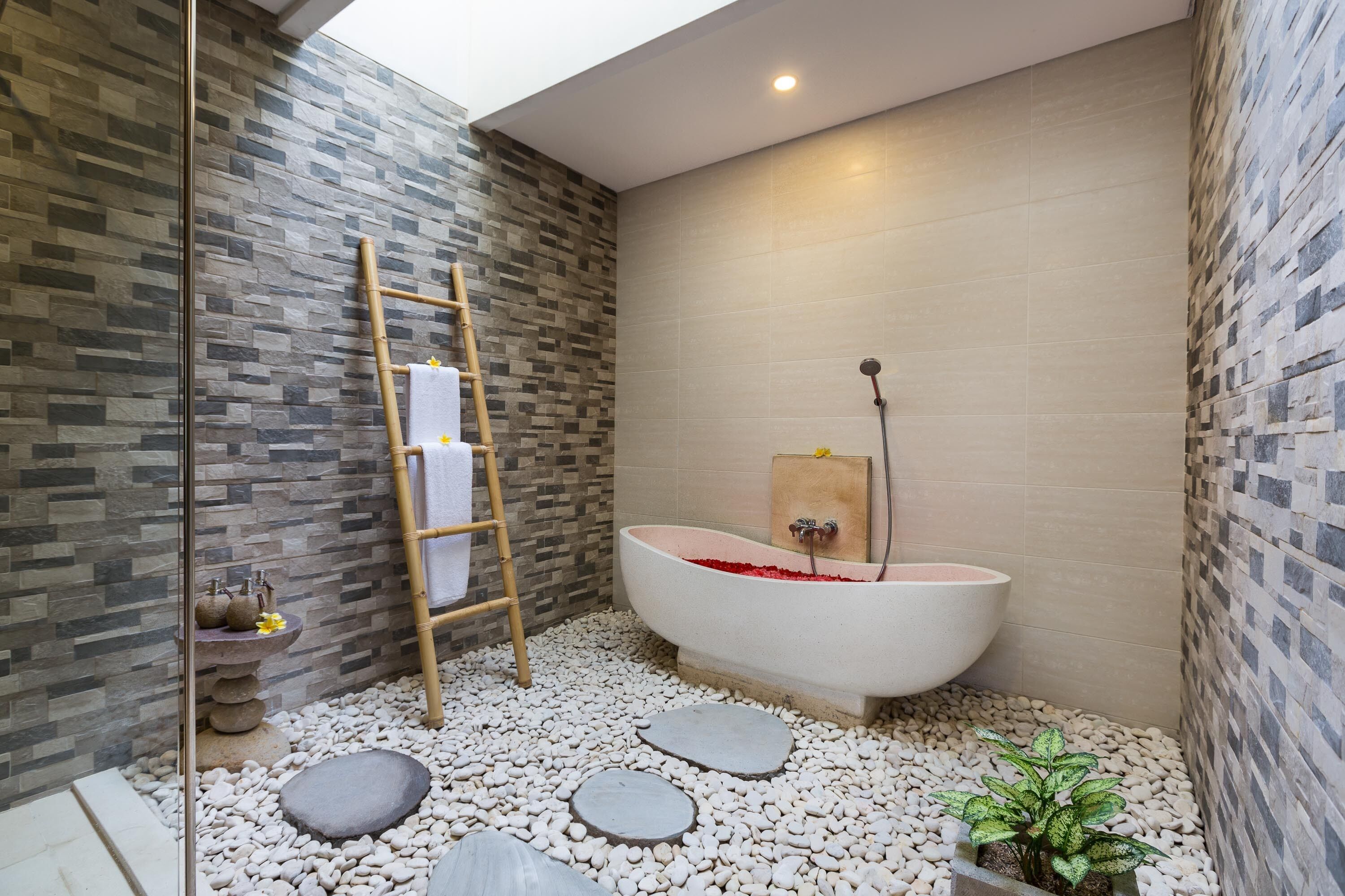 A modern bathroom with a freestanding bathtub, a wooden ladder, and a stone wall.
