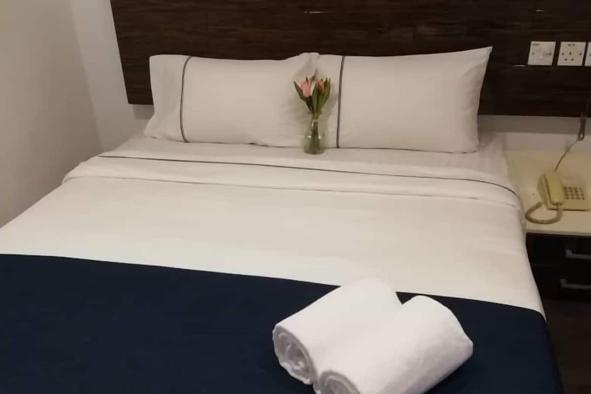 A neatly made bed with white and navy bedding, a vase with flowers, and a rolled towel on the bed.