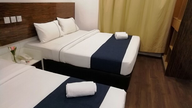 A hotel room with two beds, each with a white and navy blue bedspread, a wooden headboard, and a nightstand with a phone and a vase of flowers. - Hotel Fujisan PWTC (Kuala Lumpur)