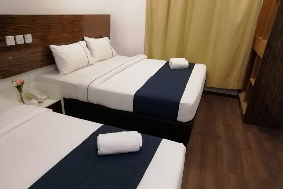 A hotel room with two beds, each with a white and navy blue bedspread, a wooden headboard, and a nightstand with a phone and a vase of flowers.