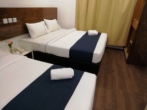 Una camera d'albergo con due letti, ognuno con copriletto bianco e blu navy, una testiera in legno e un comodino con un telefono e un vaso di fiori.